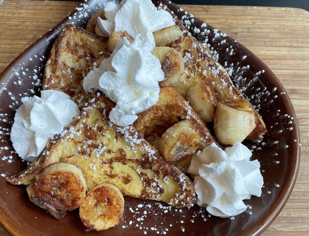 Golden-brown French toast topped with whipped cream and caramelized bananas, dusted with powdered sugar in Grand County Colorado.
